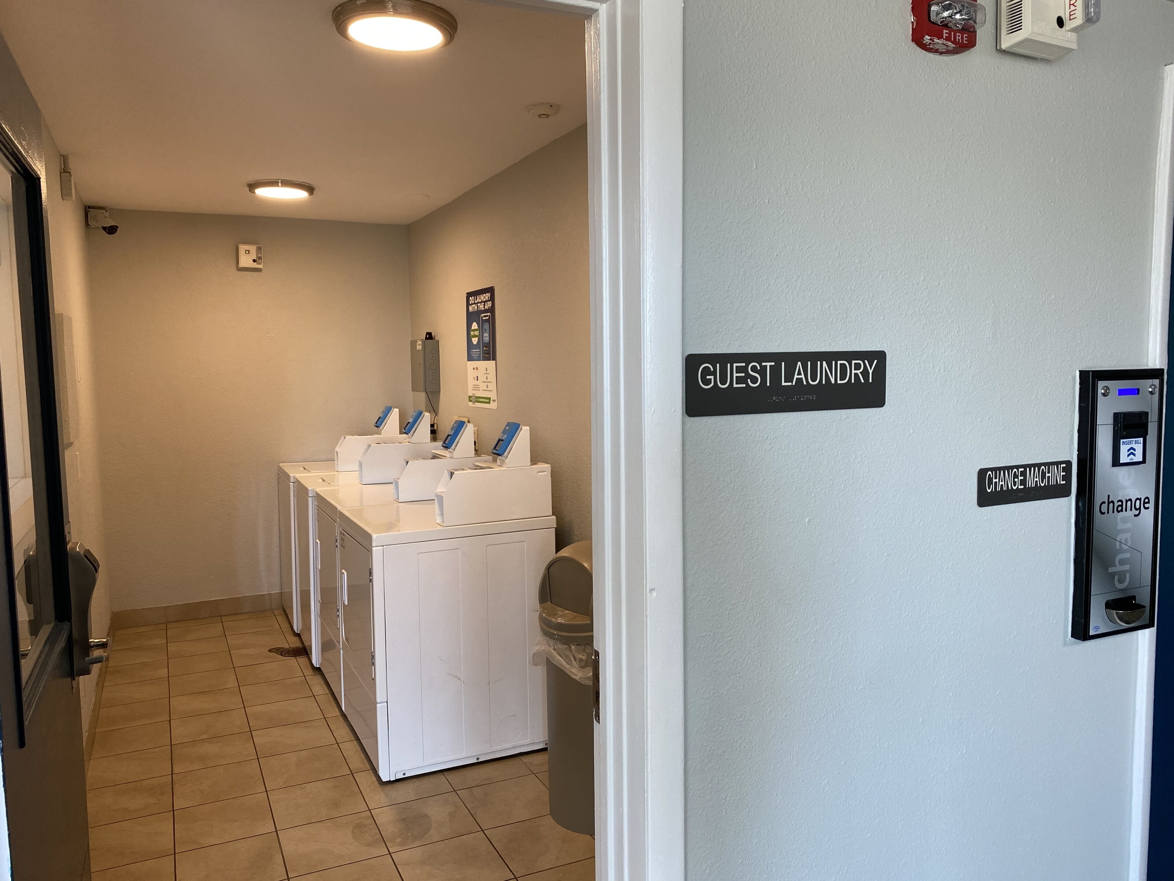A laundry area with multiple washing machines, a change machine, and a fire safety sign.