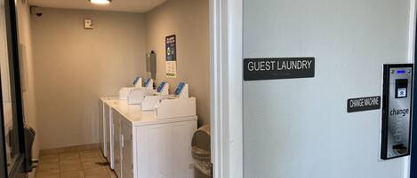 A laundry area with multiple washing machines, a change machine, and a fire safety sign.