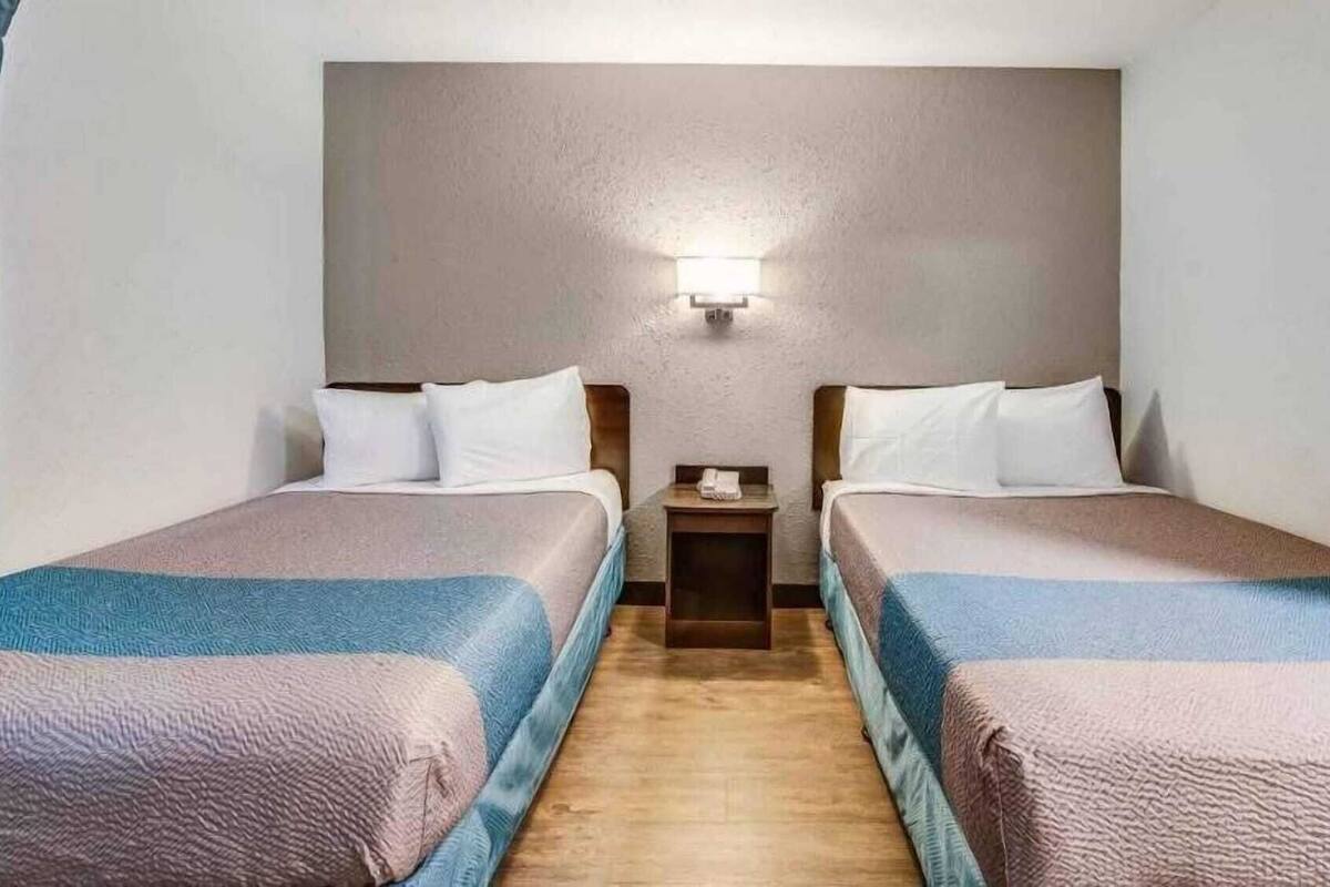 A hotel room with two beds, a nightstand, and a wall-mounted light.