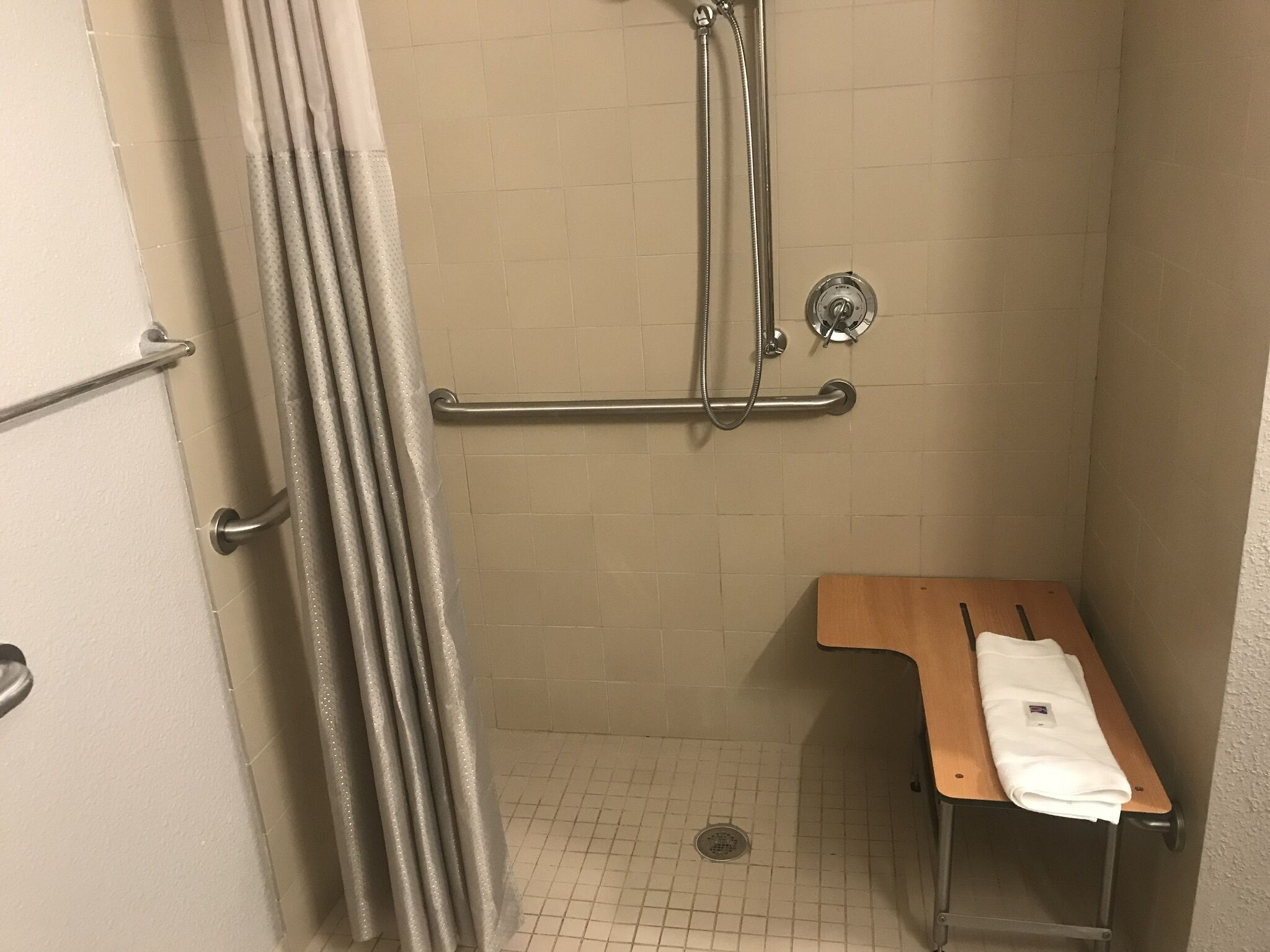 A shower area with a grab bar, a wooden bench, and a towel on it.