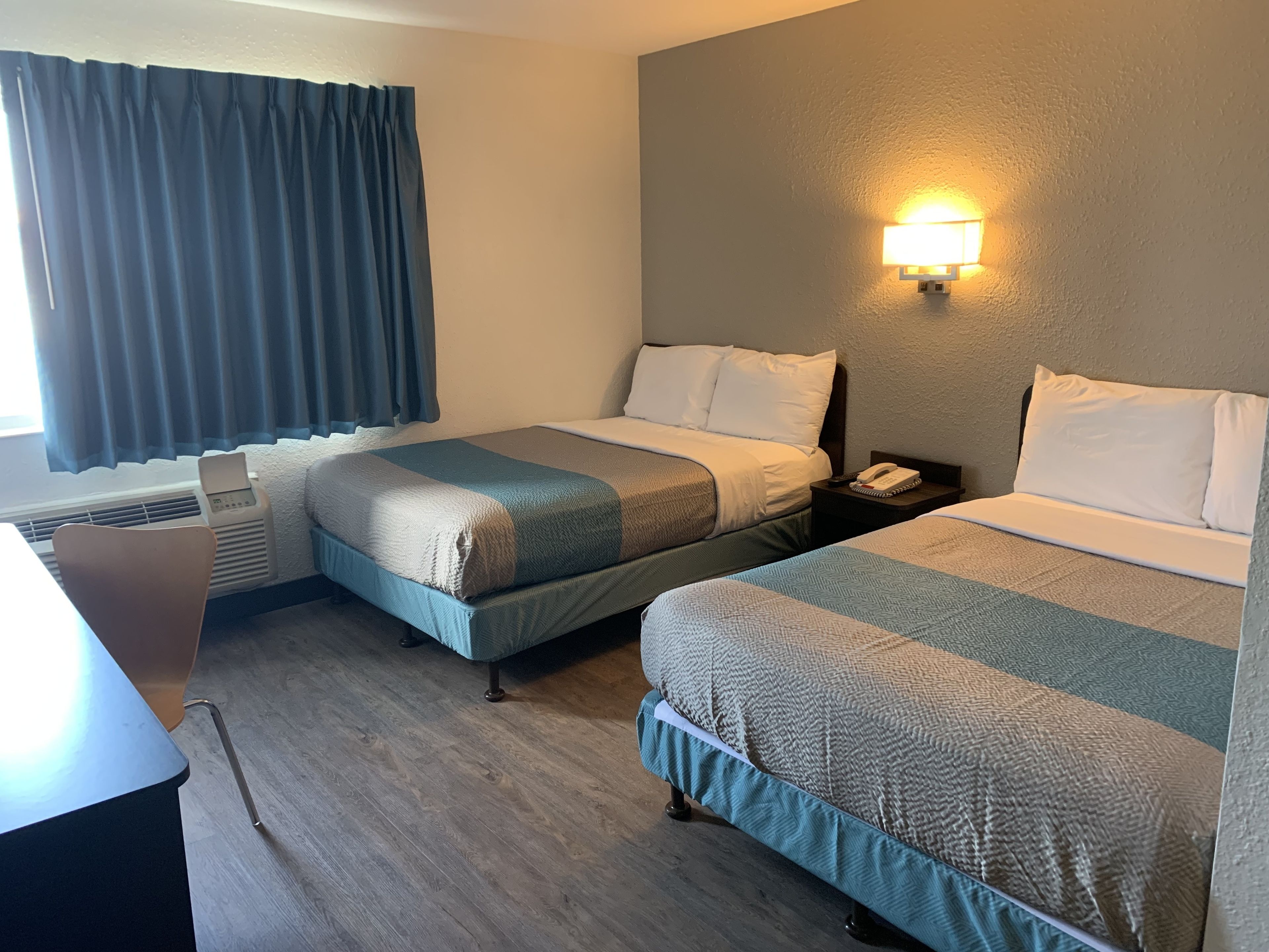 Habitación de hotel con dos camas, un escritorio, una silla, un calentador y un teléfono en la pared.