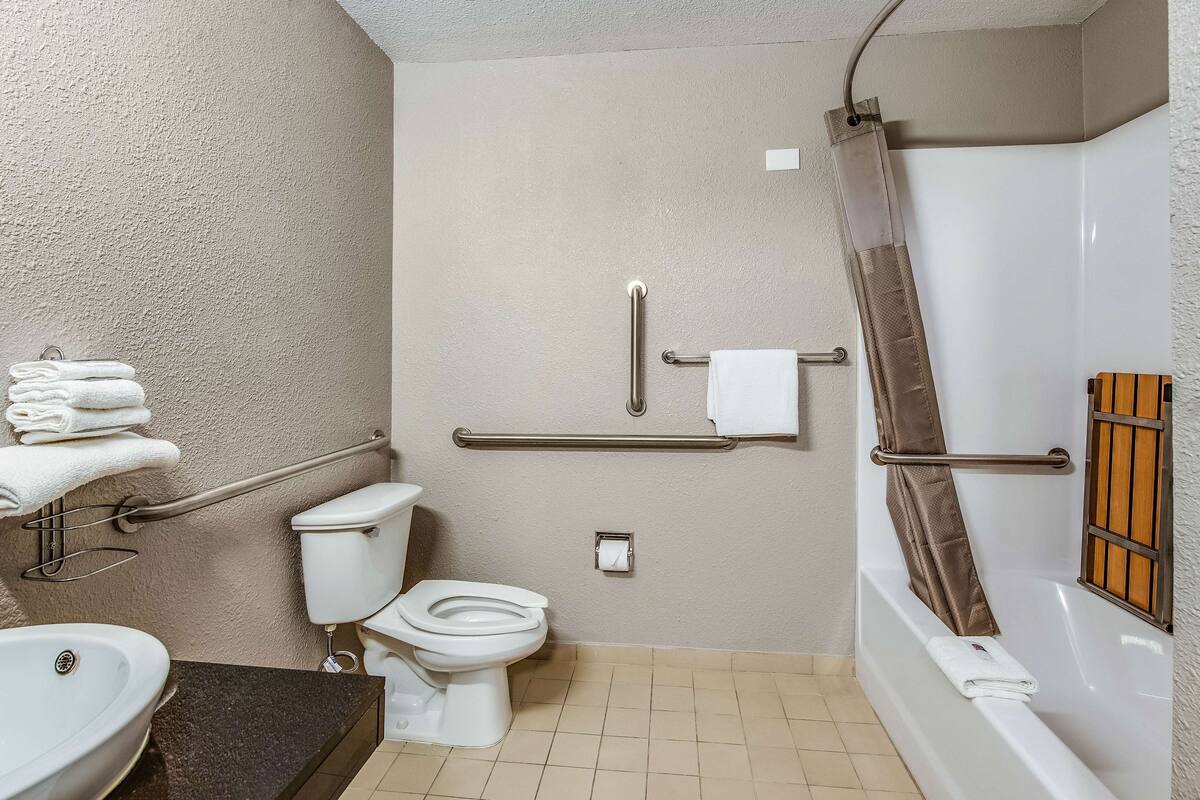 A bathroom with a toilet, sink, and bathtub. There are grab bars, a towel rack, and a shower curtain.