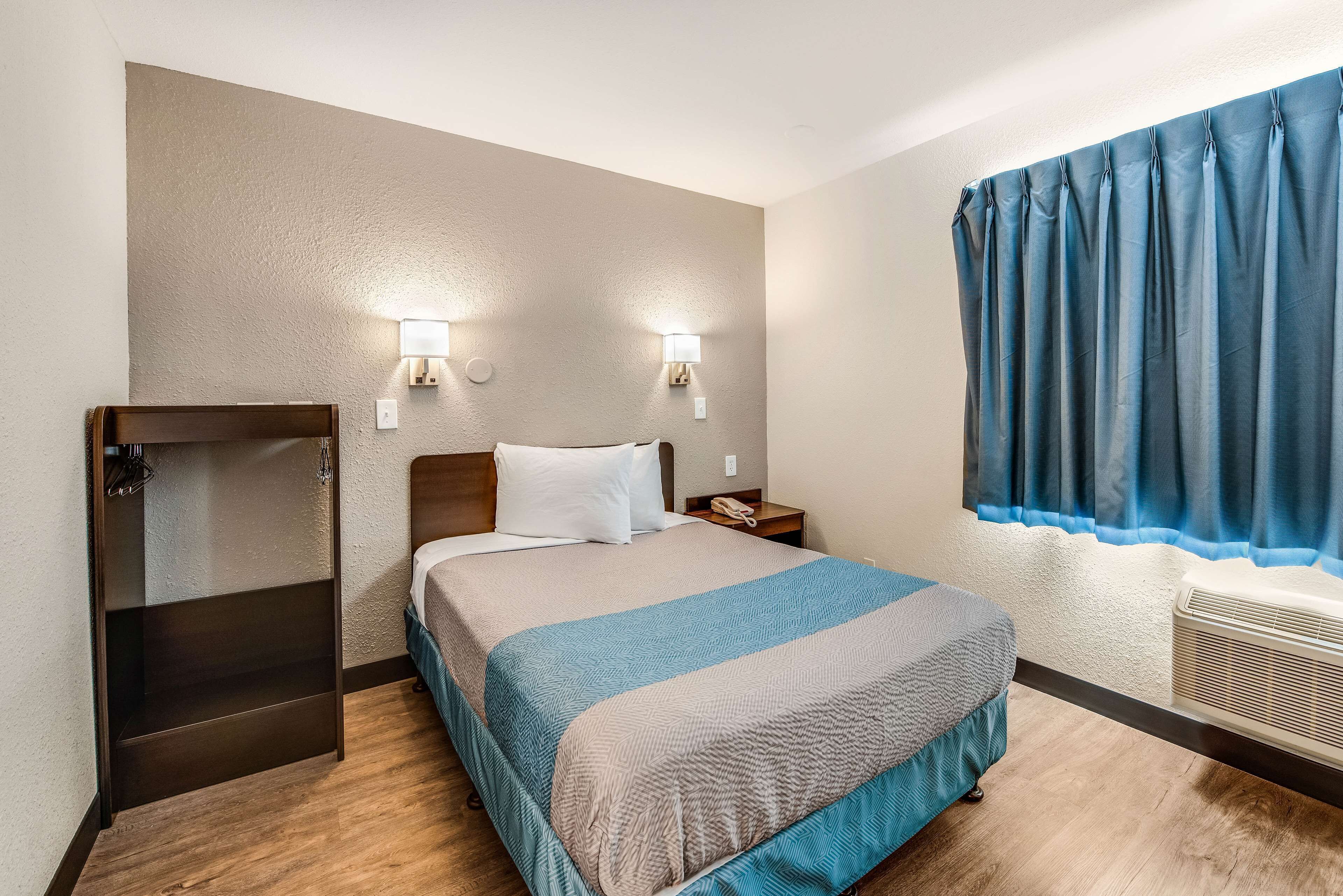 Camera d'albergo con un letto, lampade sui comodini, un armadio e una finestra con tende.