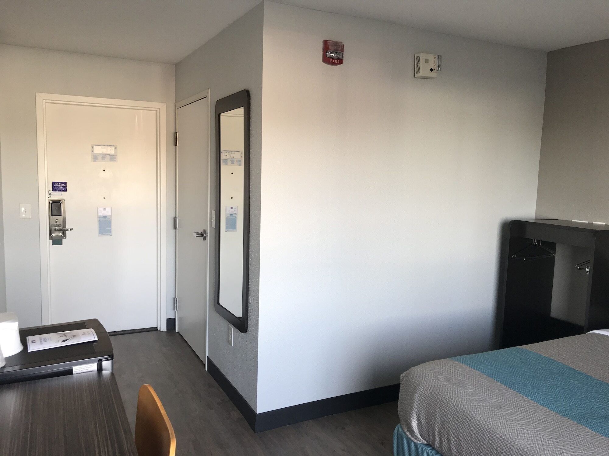 Habitación de hotel con cama, escritorio y espejo. Hay dos detectores de humo en la pared.