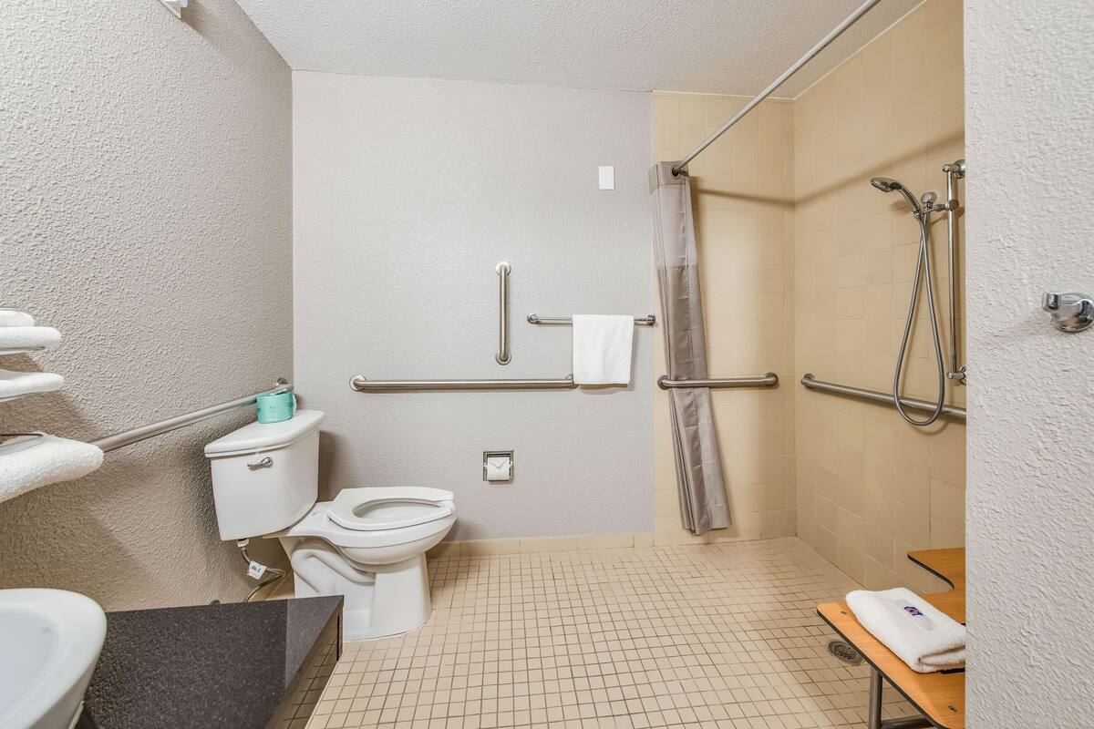 A bathroom with a toilet, a shower with grab bars, a towel rack, and a sink.