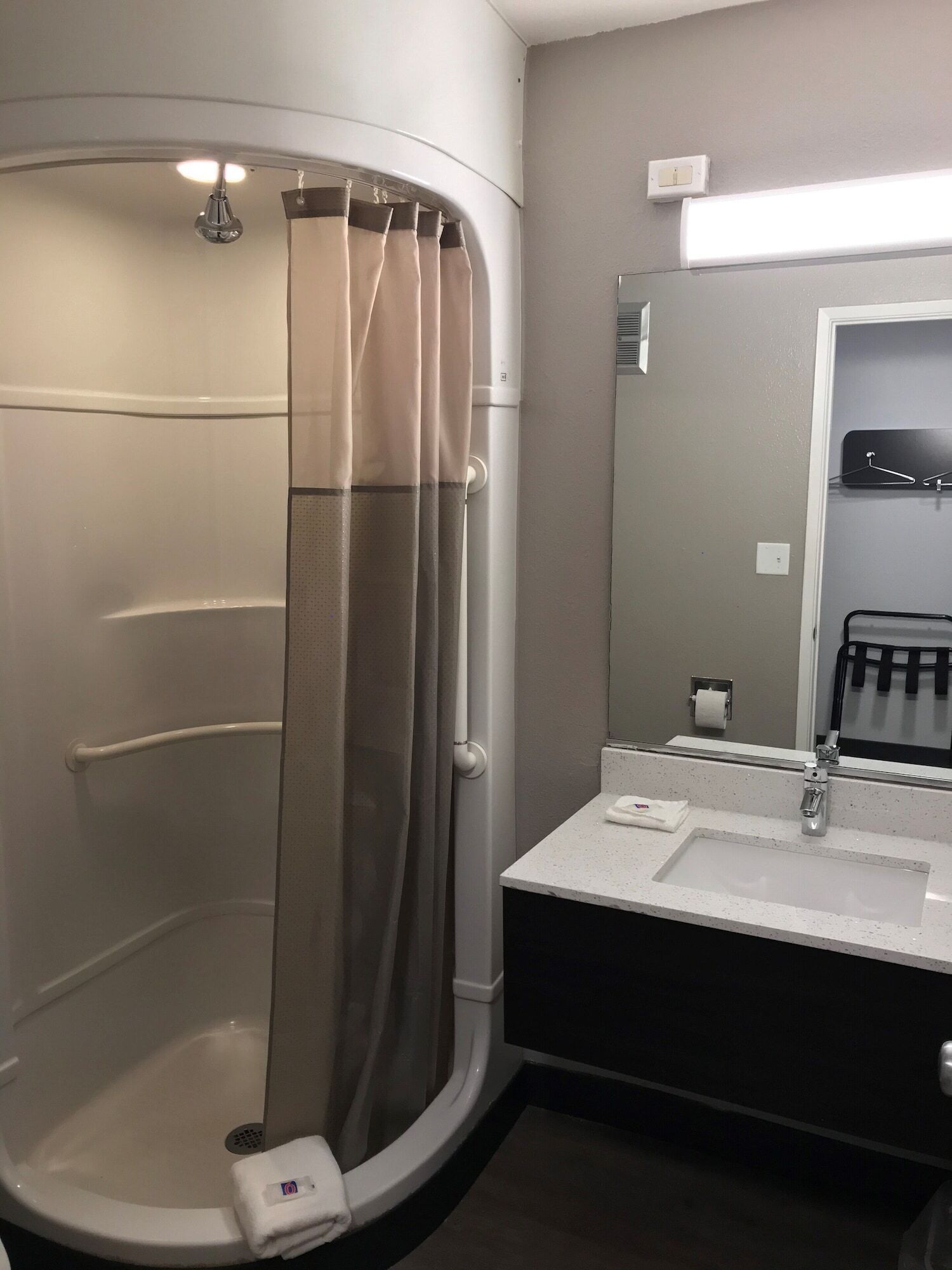 A bathroom with a shower, a sink, a mirror, and a towel rack.