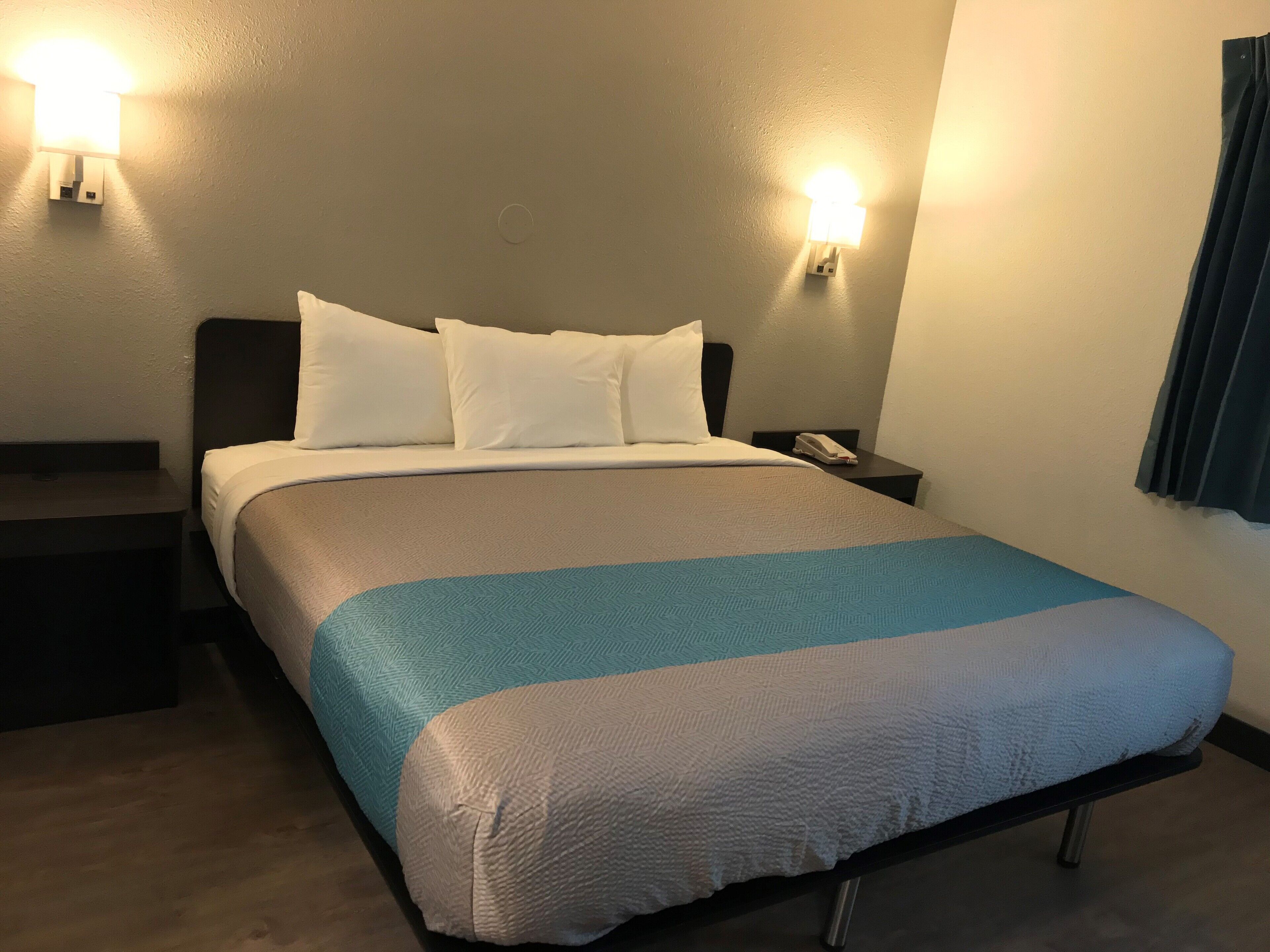 A hotel room with a bed, two bedside tables, a nightstand, and two wall-mounted lamps.