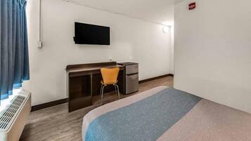 A hotel room with a bed, a desk with a chair, a television, and a small kitchenette.