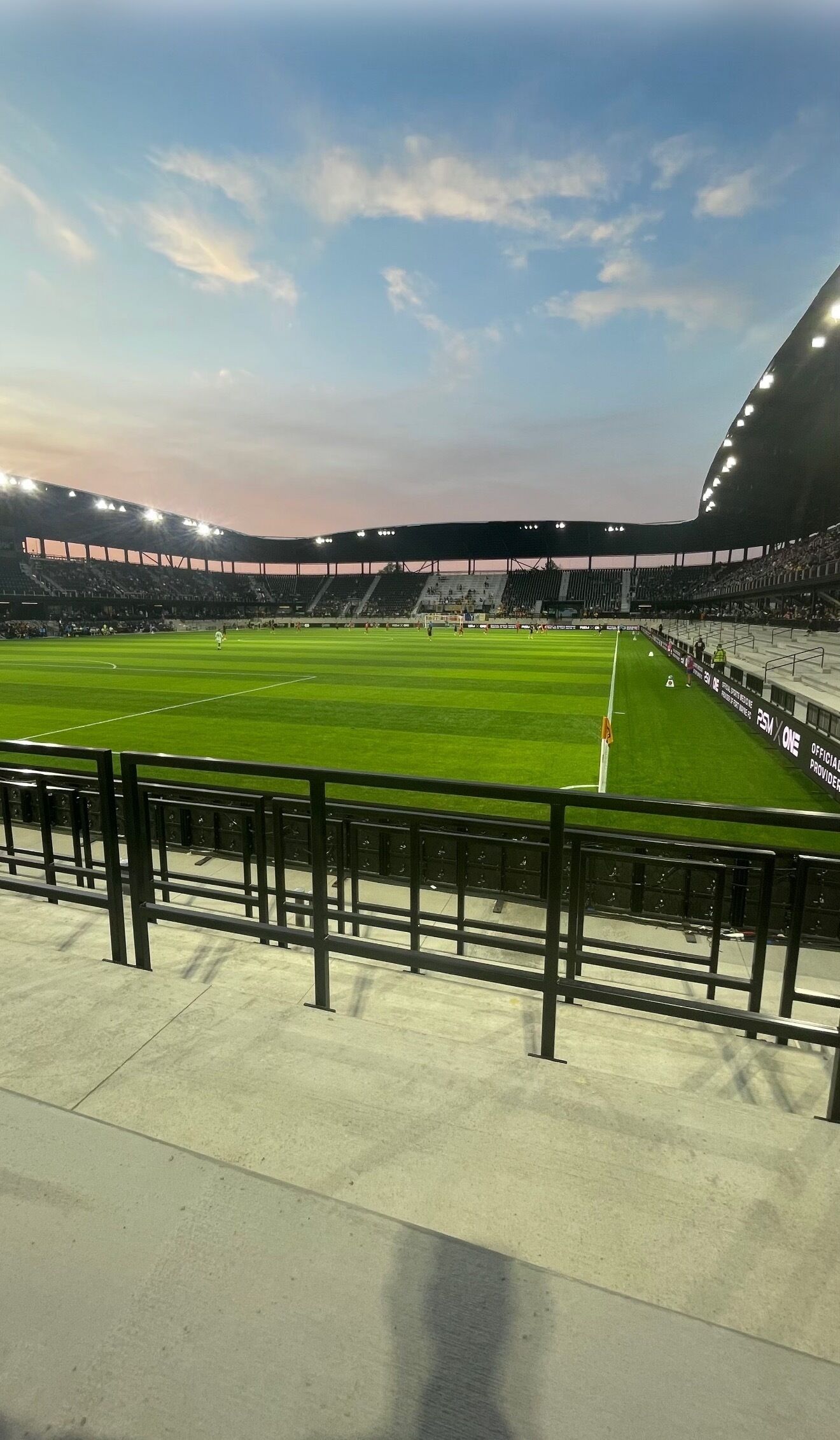 Ein Stadion mit einem grünen Rasen, Zuschauerrängen und blauem Himmel.