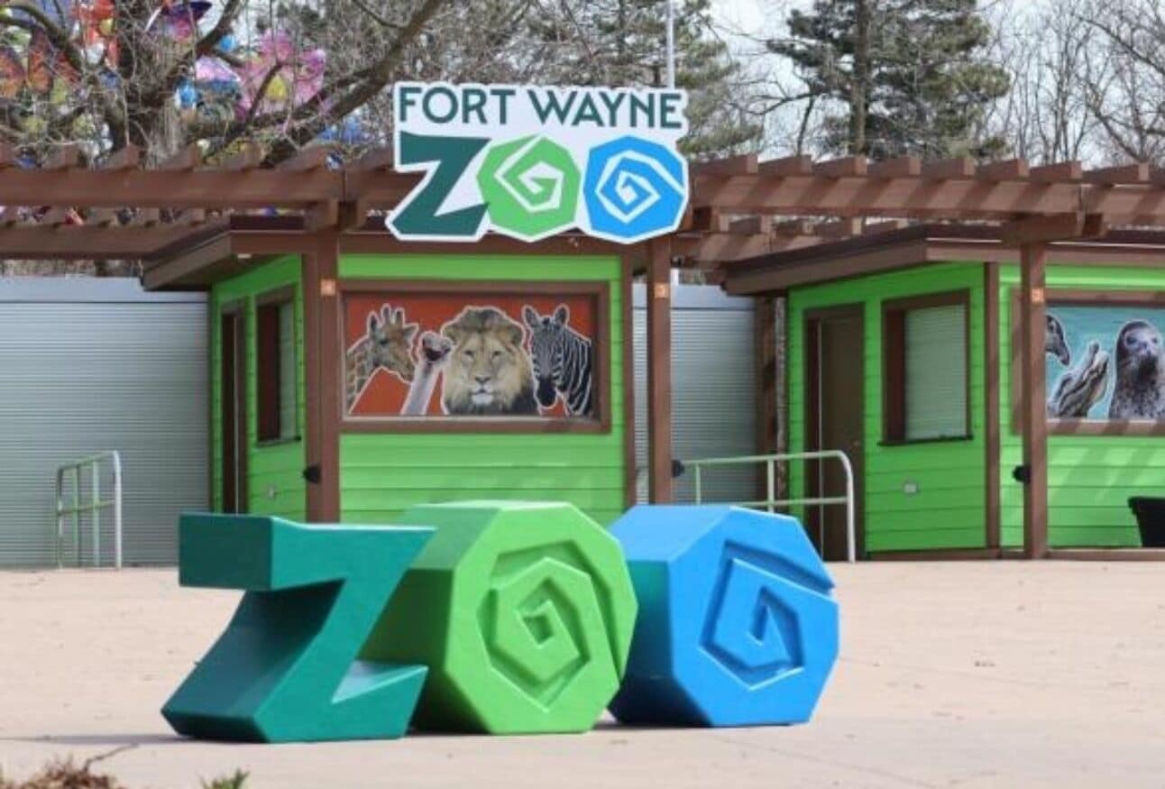 A zoo entrance with a sign, green and blue sculptures, and a mural of animals.