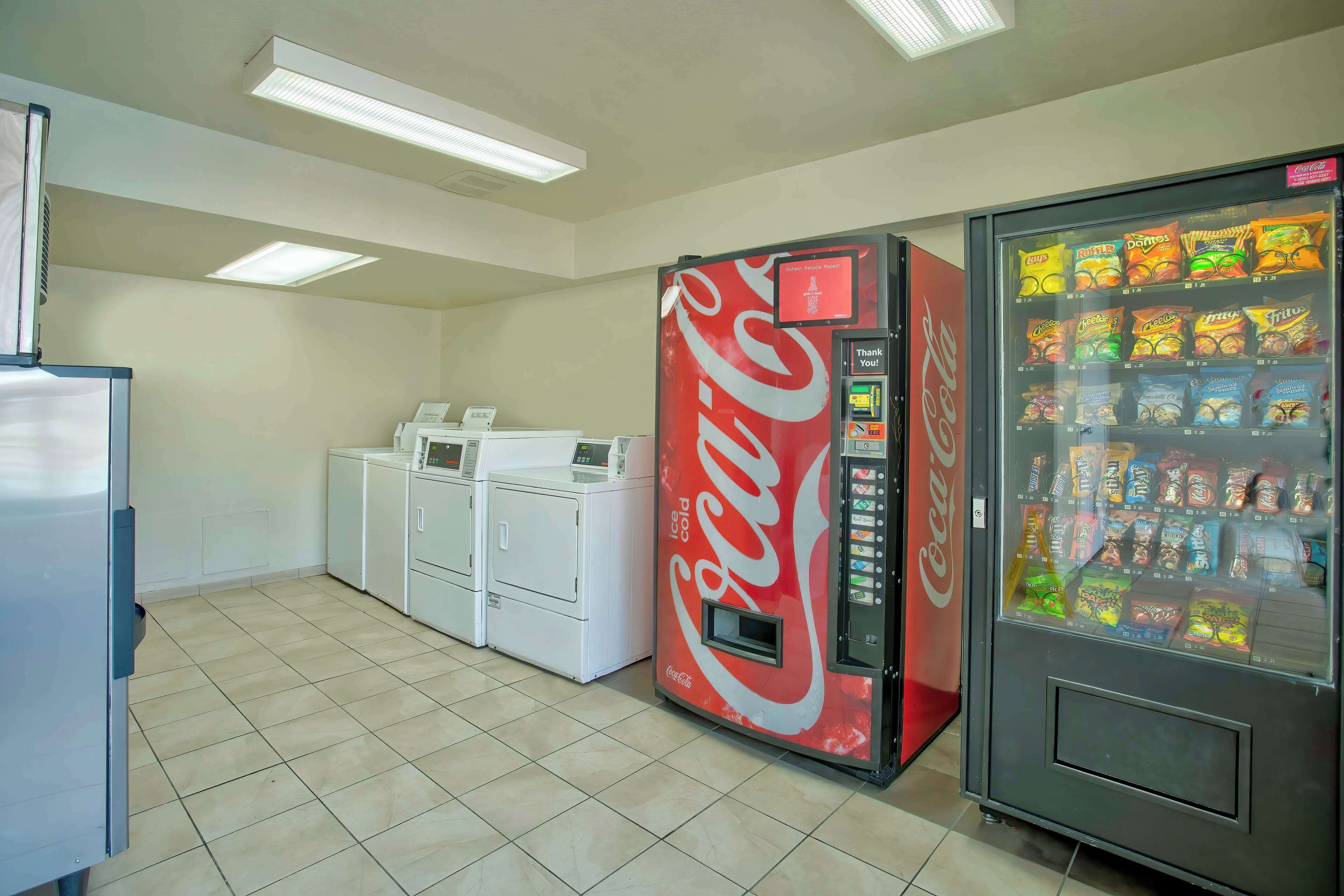 Una habitación con una máquina expendedora de Coca-Cola, una lavadora y un refrigerador.