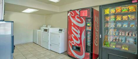 Una habitación con una máquina expendedora de Coca-Cola, una lavadora y un refrigerador.