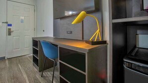Una habitación moderna con escritorio, silla, televisión montada en la pared y un cubo de basura.