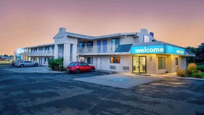 Un motel con un cartel de 'Welcome', un estacionamiento y dos coches aparcados al frente.