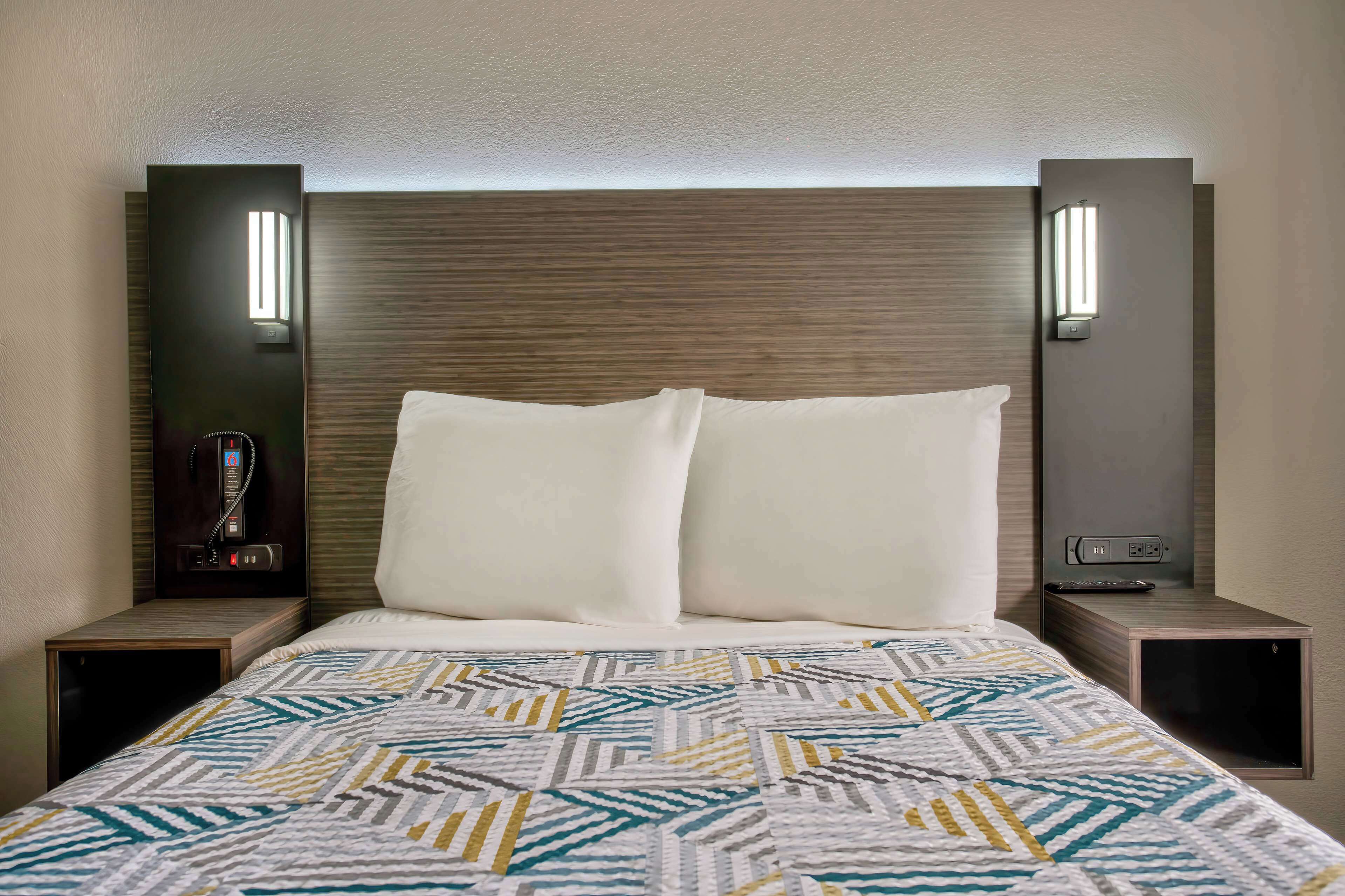 Habitación de hotel con cama, dos mesitas de noche, lámpara de pared y teléfono.