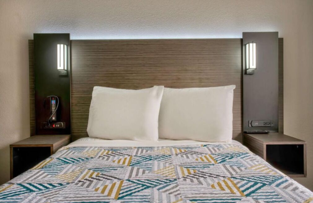 A hotel room with a large bed, two bedside tables, a wall-mounted TV, and a built-in heater.