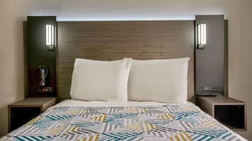 A hotel room with a large bed, two bedside tables, a wall-mounted TV, and a built-in heater.