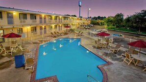 Un motel con piscina, asientos exteriores y un área de terraza cercada.