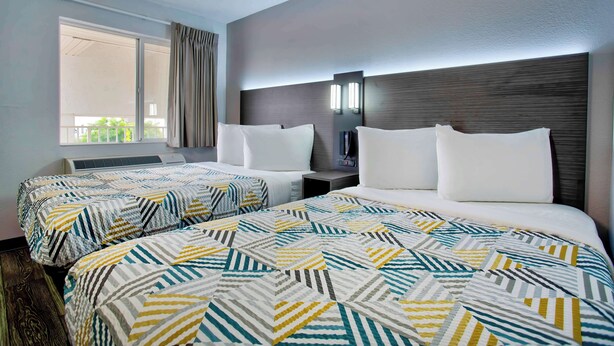 Habitación de hotel con dos camas, un ventanal grande, una mesita de noche y una lámpara fijada a la pared.