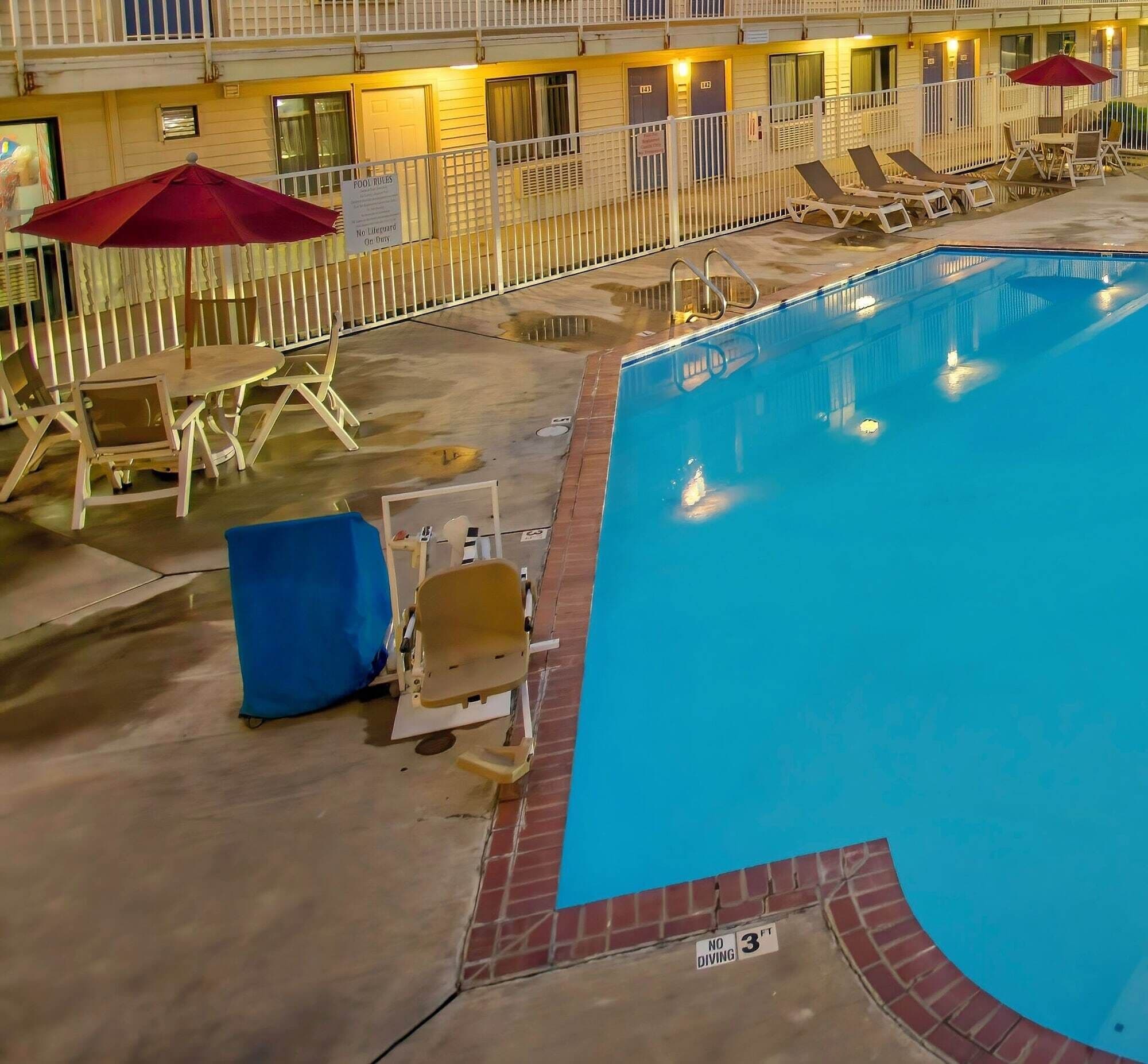 A hotel pool area with lounge chairs and umbrellas, a sign indicating no lifeguard on duty, and a diving depth warning.