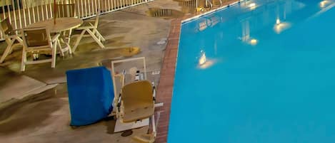 Zona de piscina hotelera con sillones reclinables y sombrillas, un letrero que indica ausencia de salvavidas y una advertencia sobre la profundidad para buceo.