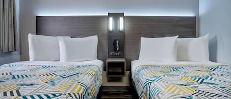 A hotel room with two beds, a nightstand with a phone, and a wall-mounted light fixture.