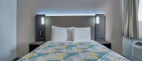 A hotel room with a bed, two bedside tables, a headboard with integrated lighting, a patterned bedspread, and a window with curtains.