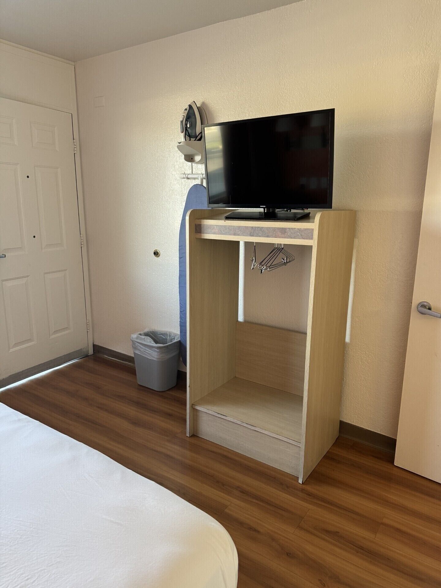 Een hotelkamer met een bed, een televisie op een houten standaard, een prullenbak en een deur.