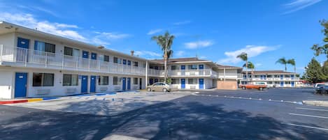 A motel with multiple rooms, a parking lot, and a clear blue sky.