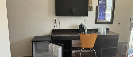 A hotel room with a bed, a desk with a chair, a television, a coffee maker, and a mini-fridge.