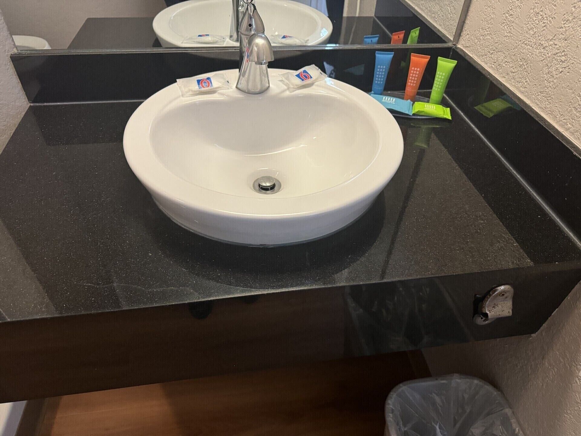 A bathroom sink with a mirror above it, a black countertop, and toiletries on the counter.