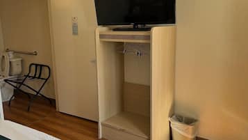 A hotel room with a bed, a television mounted on a wooden cabinet, a chair, a small table, and a trash bin.