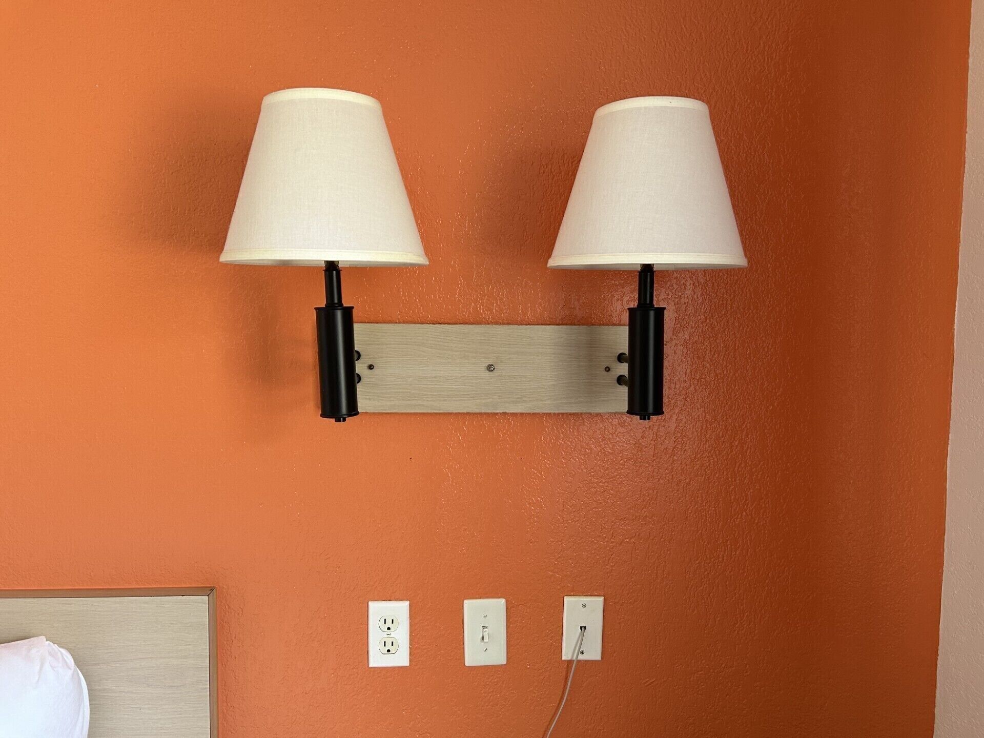 Une lampe murale dotée de deux abat-jour blancs et d’un panneau en bois.