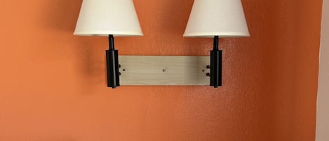 A wall-mounted lamp with two white lampshades and a wooden panel.