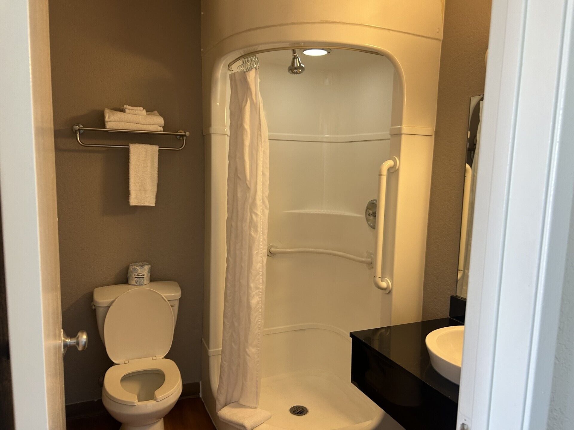 Un baño con inodoro, ducha con cortina blanca, lavabo y toallero con toallas.