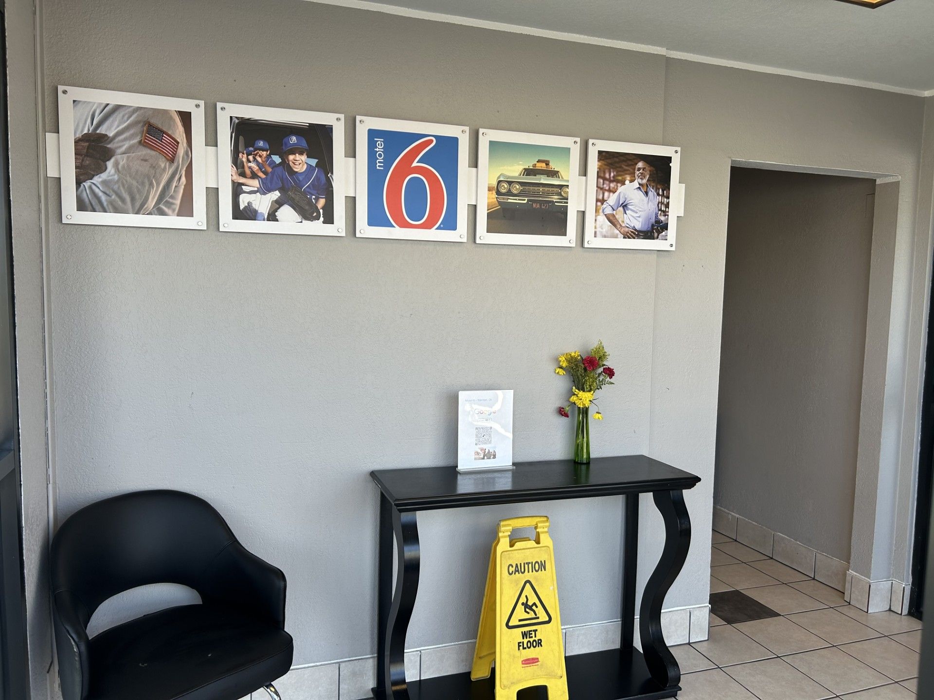 Eine Wand mit gerahmten Fotos, ein schwarzer Tisch mit Blumen in einer Vase und ein Warnschild auf dem Boden.