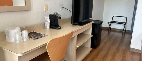 A hotel room with a wooden desk, a television, a coffee maker, and a trash bin.