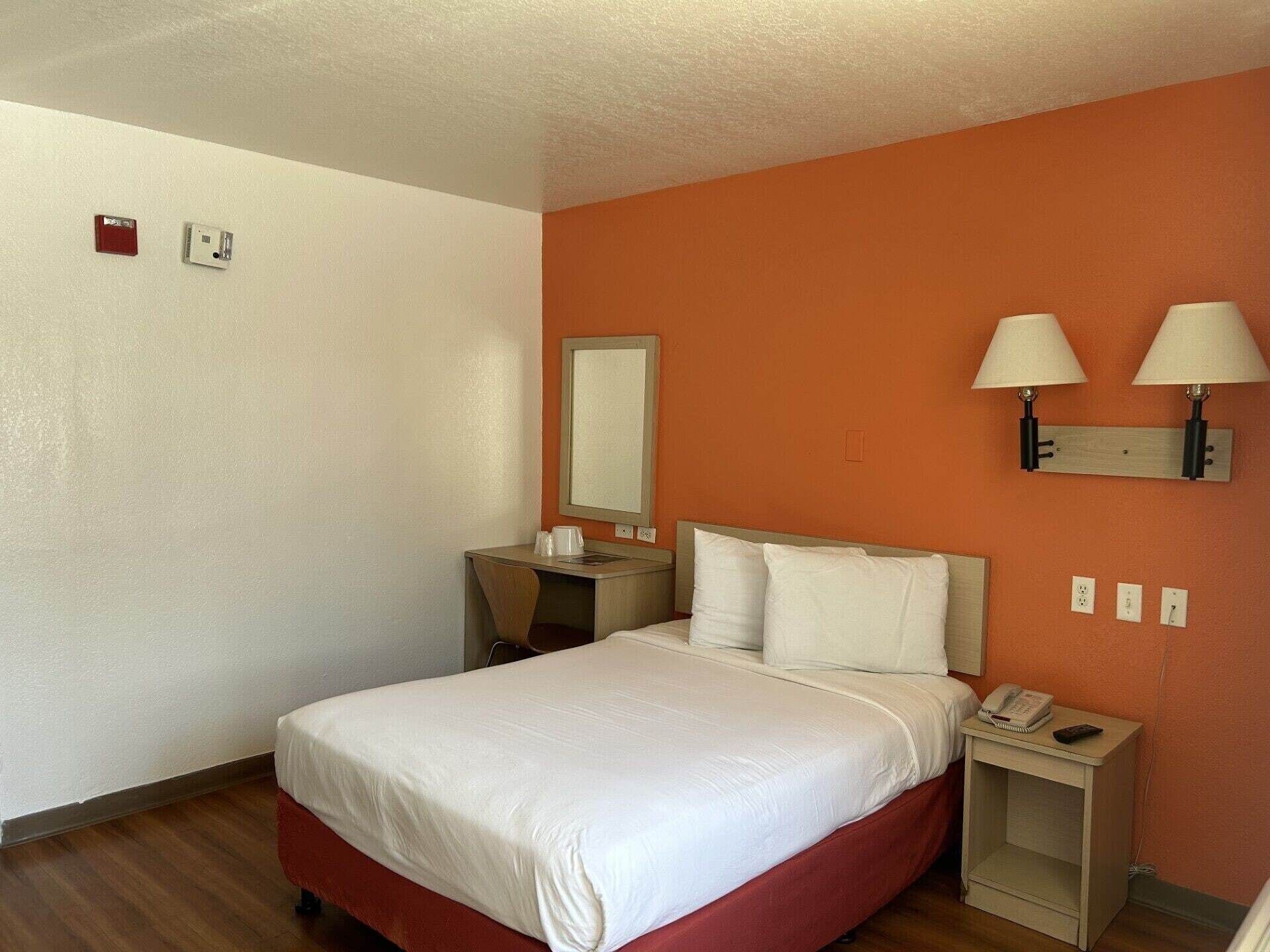 A hotel room with a bed, bedside table, lamp, and a mirror on the wall.