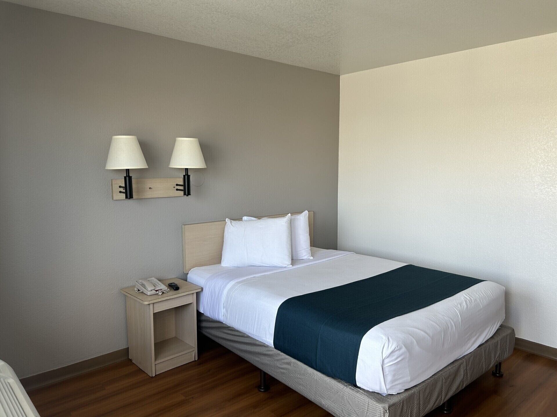 Una habitación de hotel con una cama, una mesita de noche con un teléfono y dos lámparas de pared.