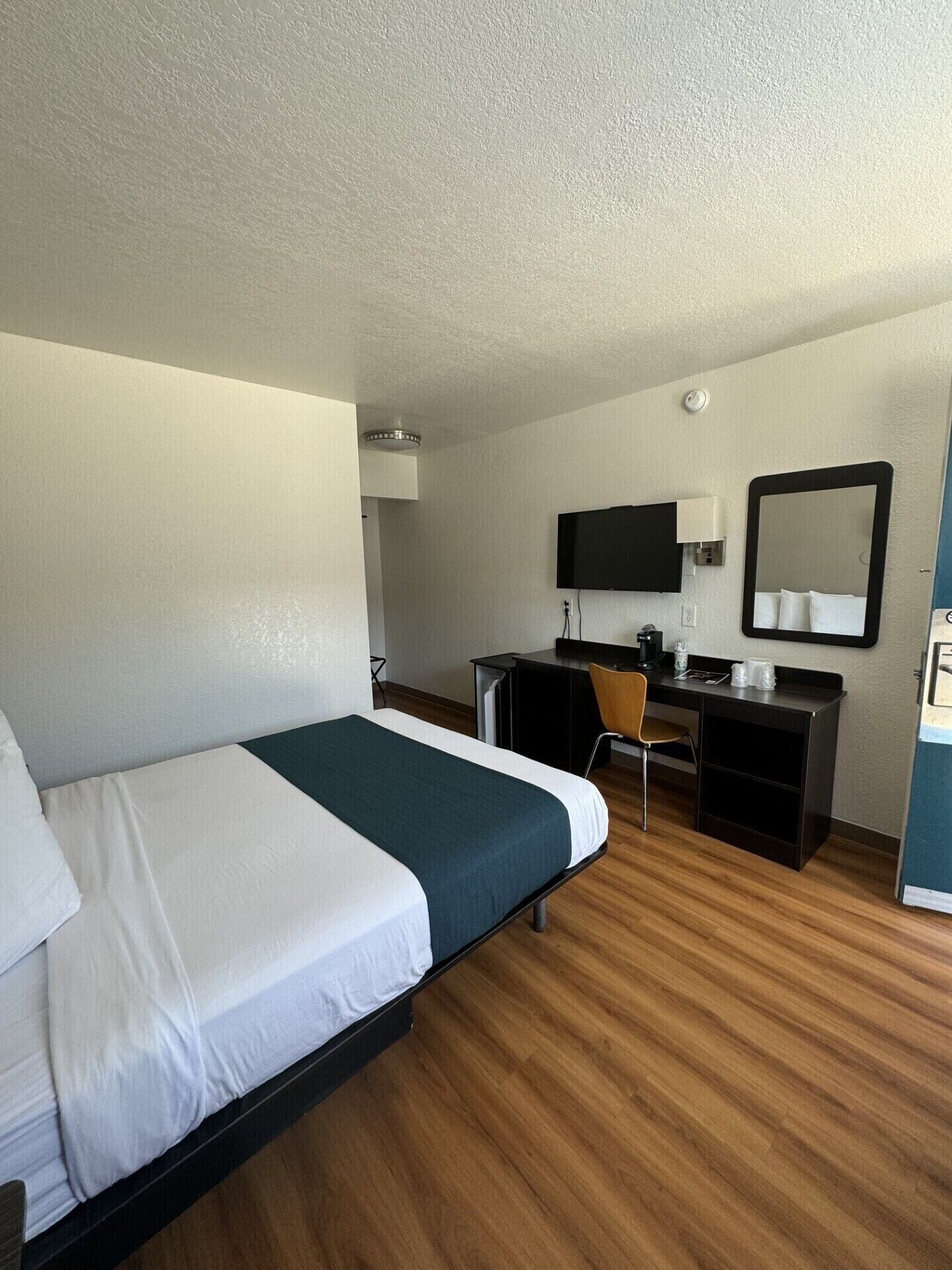 A hotel room with a bed, a desk, a chair, a TV, and a mirror.
