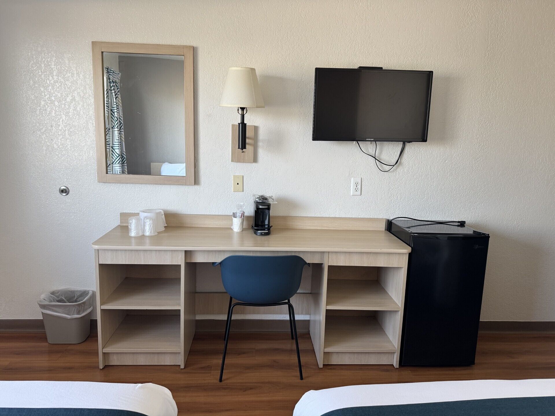 Habitación de hotel con un escritorio de madera, una silla azul, un televisor, un cubo de basura y dos camas.