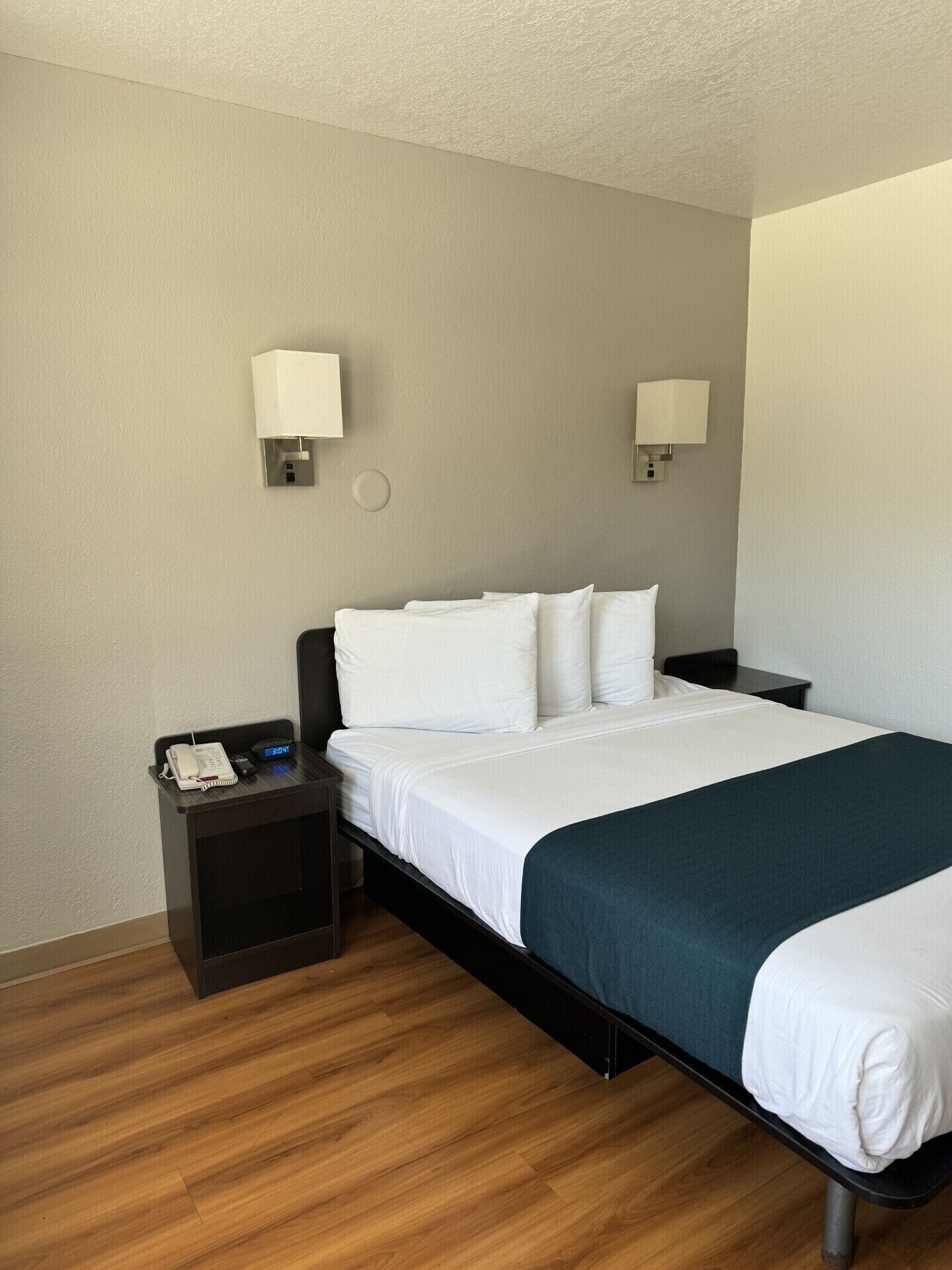 A hotel room with a bed, two bedside tables, a nightstand, and two wall-mounted lamps.