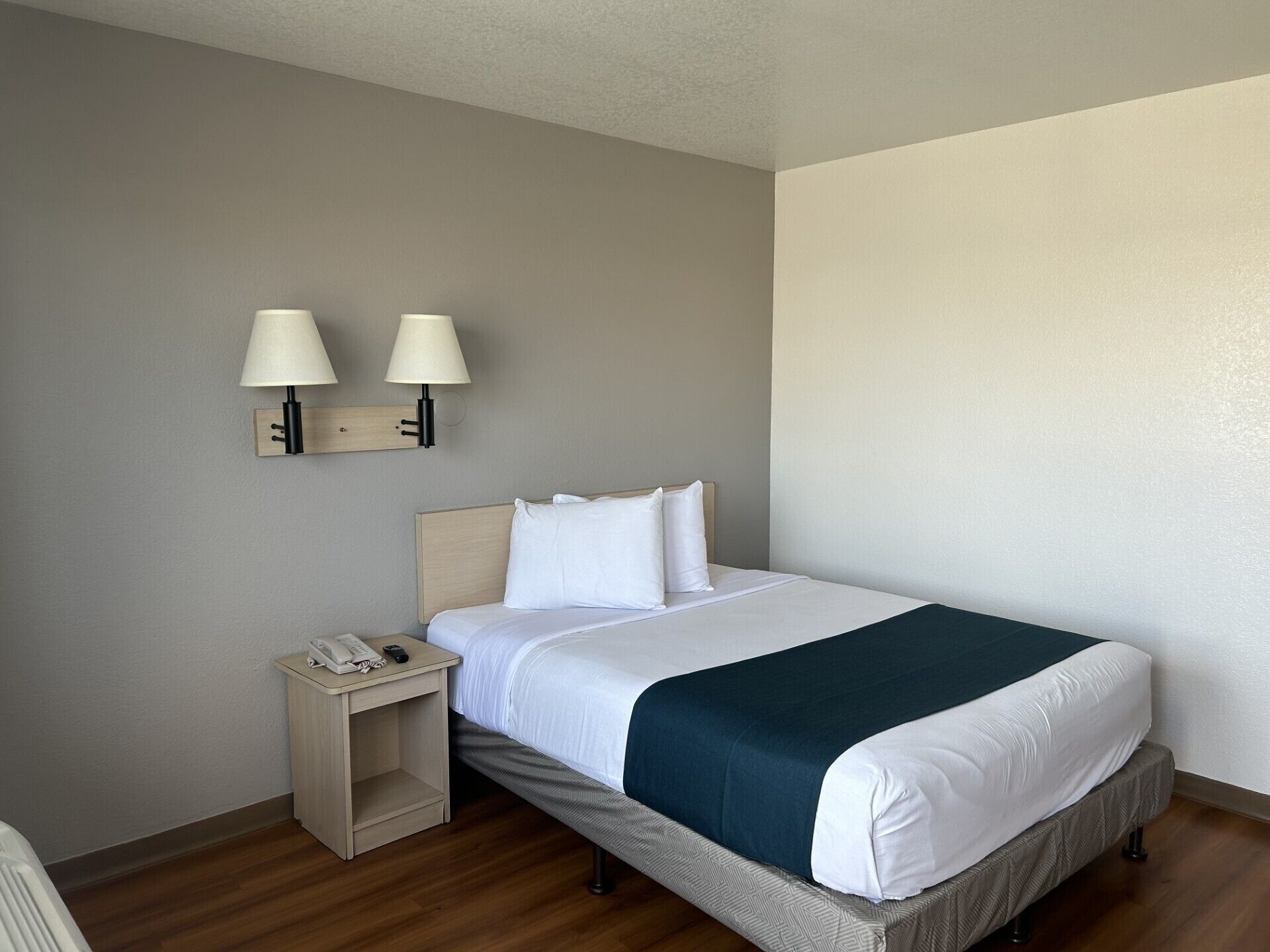 A hotel room with a bed, bedside table, lamp, and a telephone.