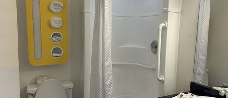 A bathroom with a white toilet, a sink with a black countertop, a shower with a checkered curtain, and a yellow towel rack with three towels.
