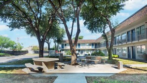 A courtyard with outdoor seating, trees, and a building with multiple windows and balconies. - Motel 6 Del Rio, TX (Del Rio)