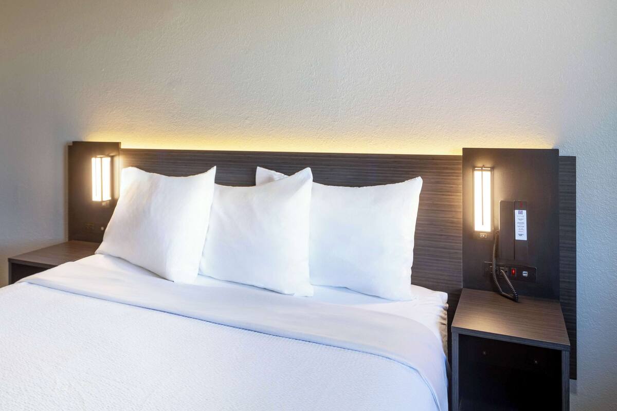 A neatly made bed with white linens, flanked by two bedside tables with built-in lamps.
