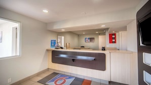A hotel reception area with a counter, a digital screen, and a fire safety sign. - Motel 6 Del Rio, TX (Del Rio)
