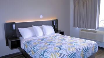 Een net opgemaakt bed met een beddengoed met patroon, twee nachtkastjes met lampen, een wandlamp en een raam met gordijnen.