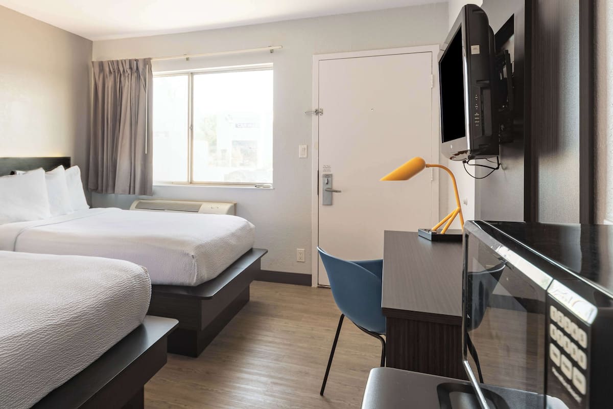 A hotel room with two beds, a desk with a TV, a chair, and a window with curtains.