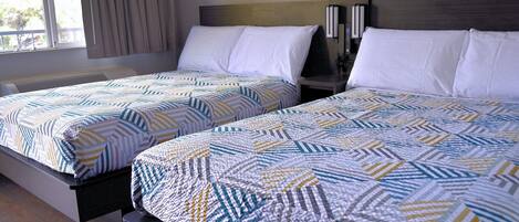 A hotel room with two beds, each with a patterned bedspread and white pillows.